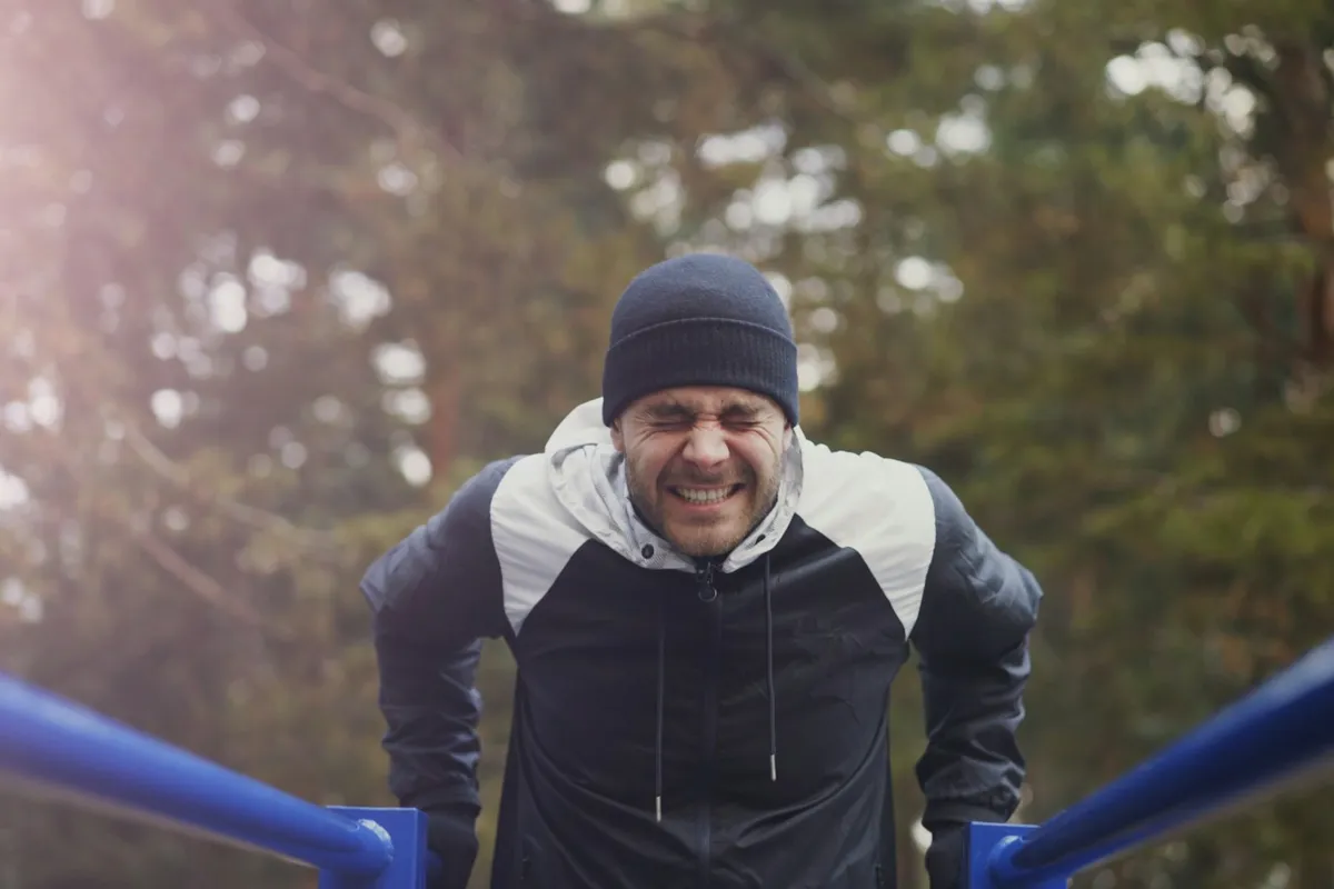 A man on outdoor parallel bars with his arms bent at the bottom of a dip