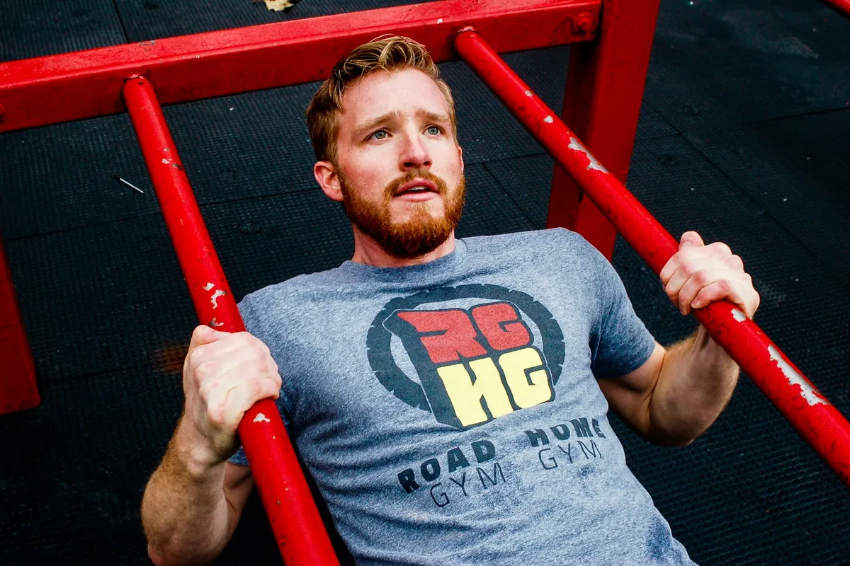 A man's hands gripping a red bar overhead in a gym
