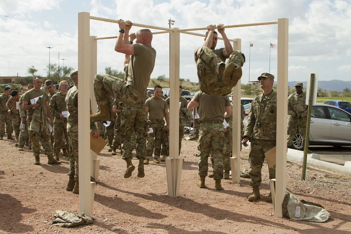 Two soldiers hanging from a bar in an outdoor fitness test, knees drawn up toward their chests
