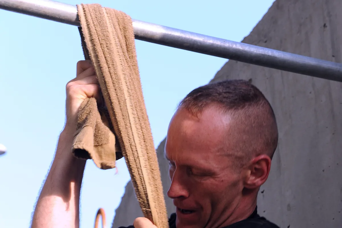 A man pulling himself up on a towel looped over a bar