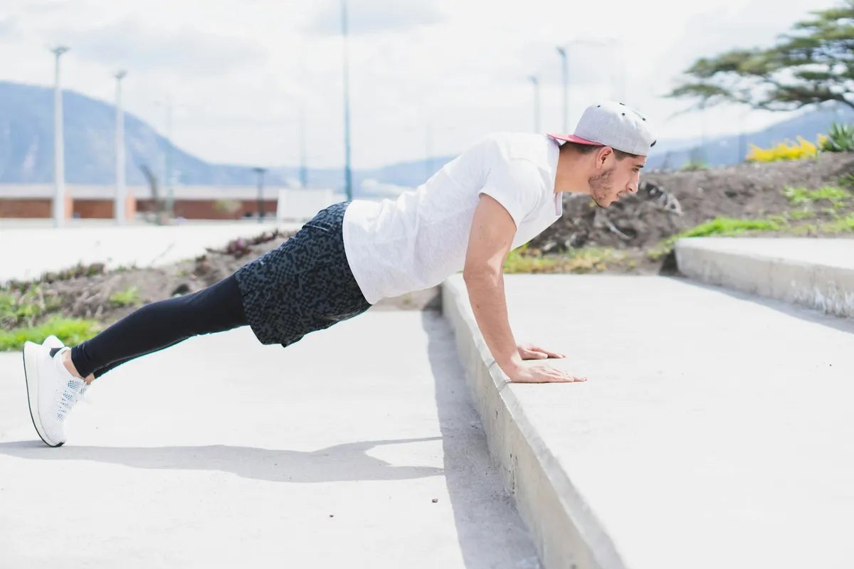 A man doing an incline push-up with his hands on a concrete ledge outdoors