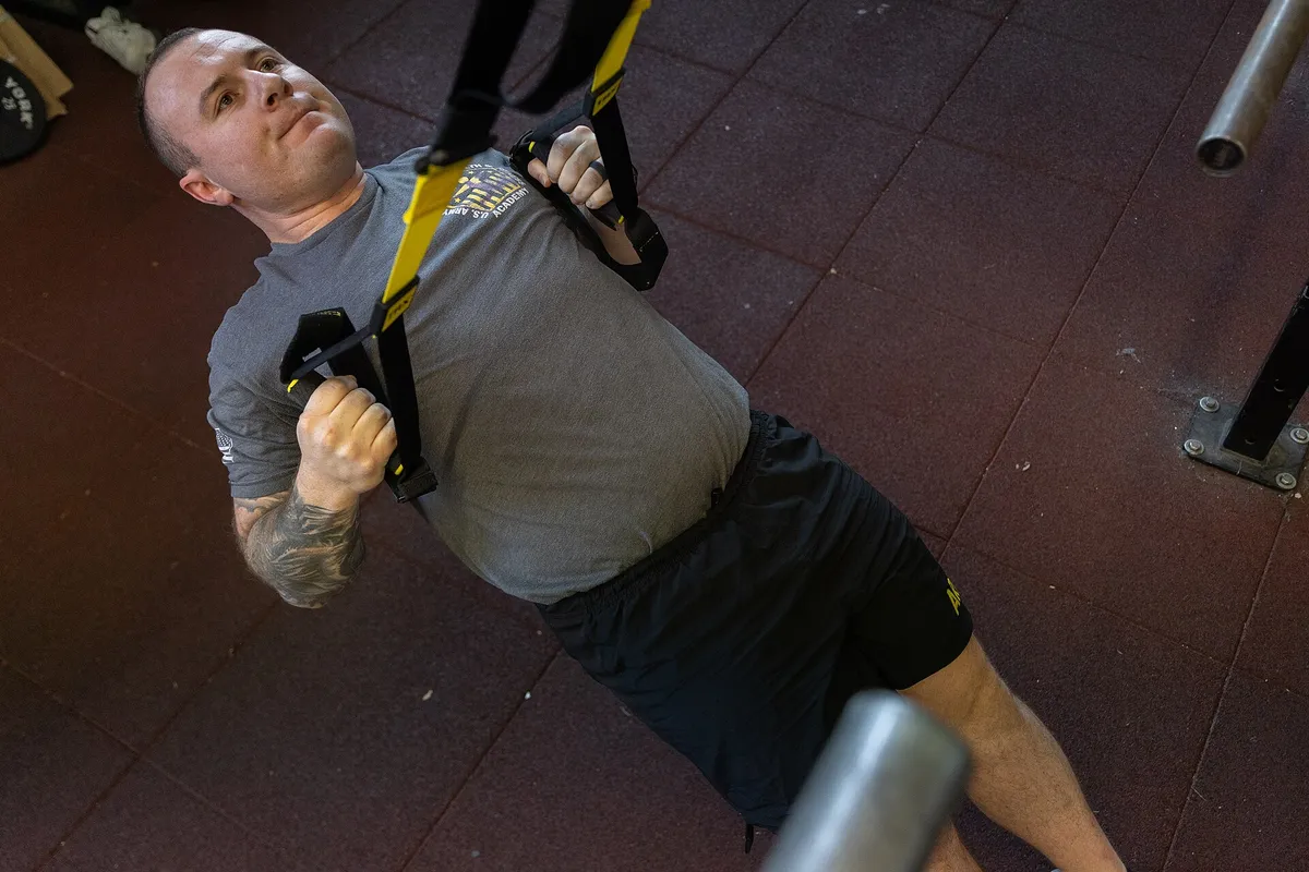 A man leaning back on suspension straps at the top of an inverted row, body in one straight line