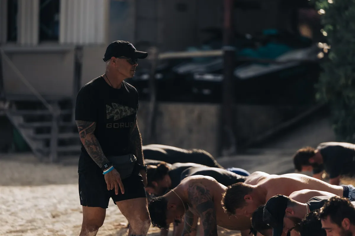 A row of people holding the bottom of a push-up on the ground while an instructor stands over them