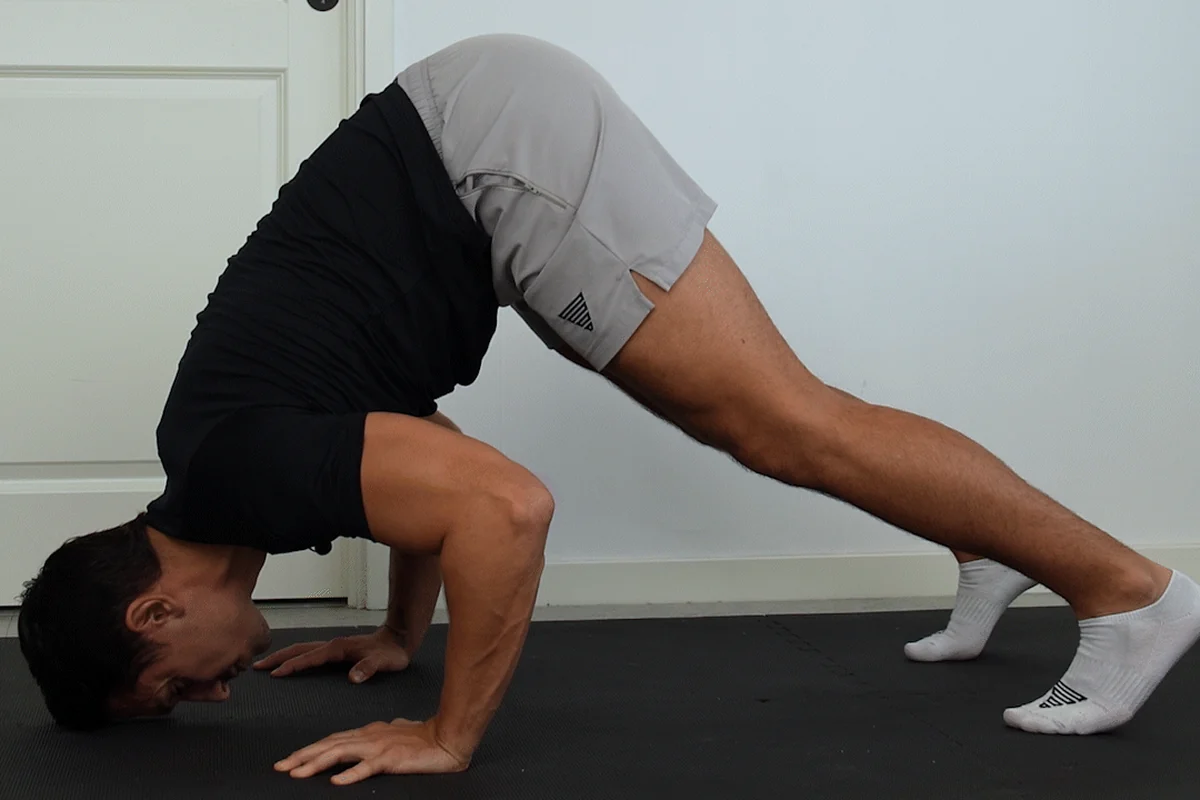 A man at the bottom of a pike push-up, hips high, head lowered to the floor in front of his hands