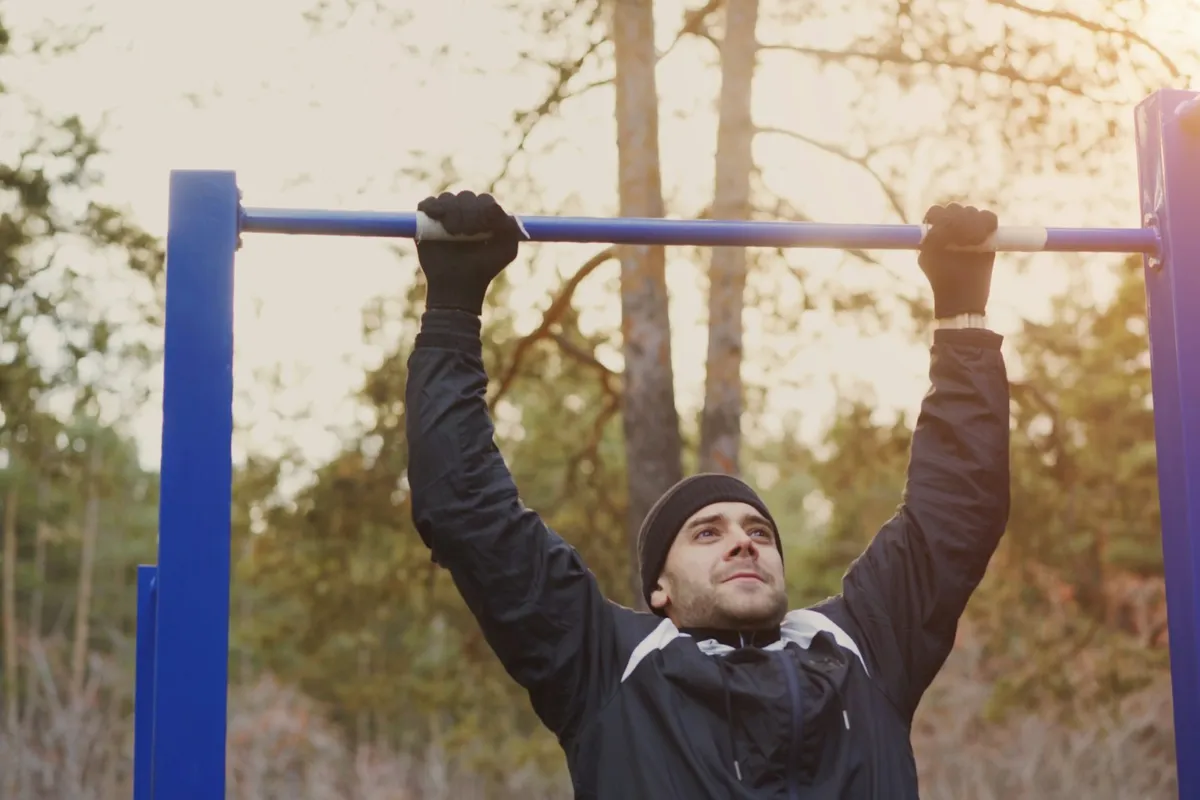 A man hanging from an outdoor pull-up bar with straight arms