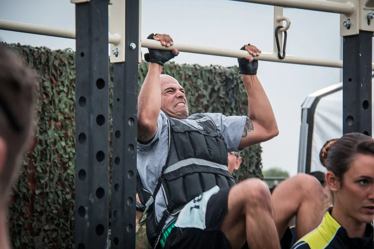 A man in a weighted vest pulling himself up on a bar at an outdoor rack